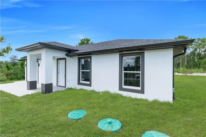 View of side of home featuring a lawn, stucco siding, roof with shingles, and a patio