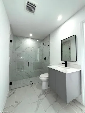 Bathroom with light marble finish flooring, vanity, a marble finish shower, and recessed lighting