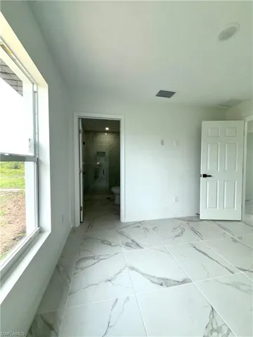 Unfurnished bedroom with light marble finish floors and connected bathroom