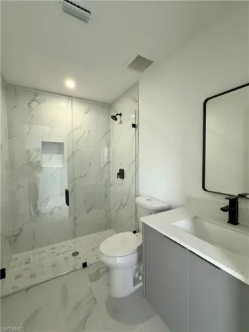 Bathroom with vanity, a marble finish shower, and marble look tile flooring