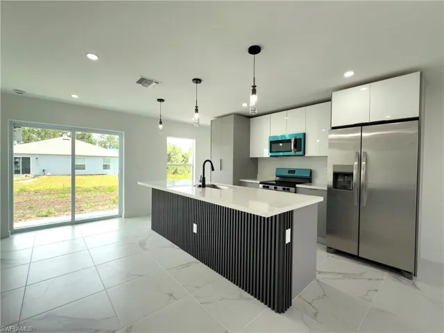 Kitchen with light marble finish floors, stainless steel appliances, pendant lighting, an island with sink, and recessed lighting