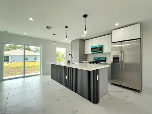 Kitchen with stainless steel appliances, light marble finish floors, pendant lighting, a center island with sink, and recessed lighting
