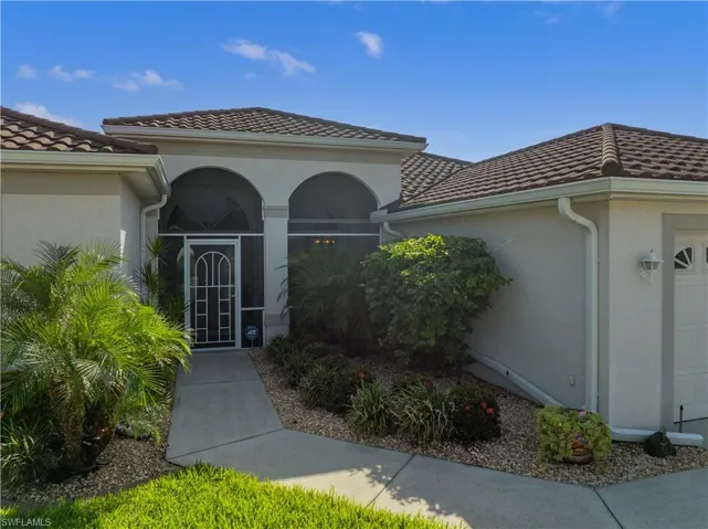 Tiled roof lines, stucco exterior, screened front entry, arched architectural details, and mature landscaping