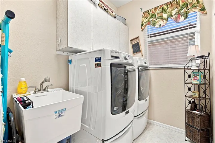 Laundry room featuring a utility sink, wall-mounted cabinetry, and a window with horizontal blinds