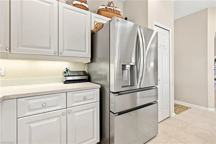 White cabinetry with under-cabinet lighting, light-toned countertop, stainless steel French-door refrigerator, and light-toned tile flooring