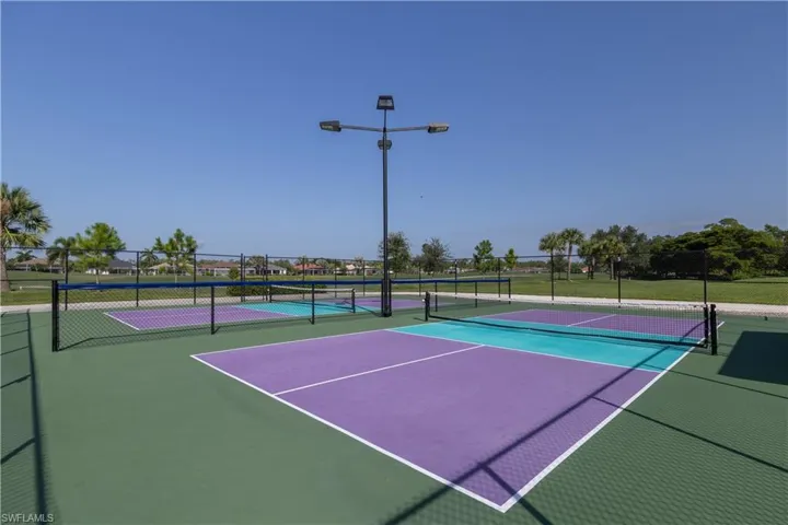 Pickleball courts with green, purple, and blue surface markings, perimeter fencing, and overhead lighting