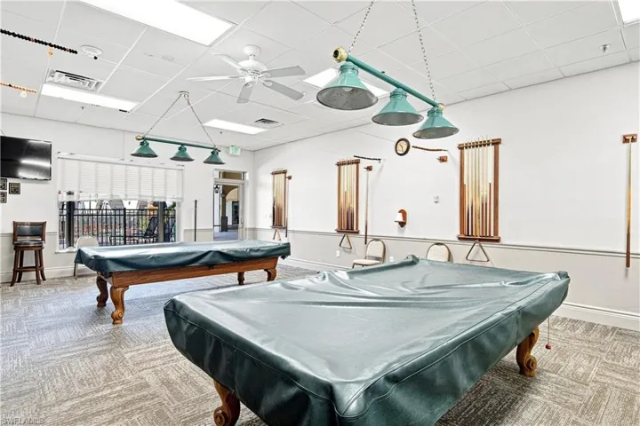 Recreational room featuring two billiard tables with overhead lighting, patterned carpet flooring, and window blinds