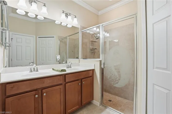Bathroom featuring crown molding, double vanity, and a shower stall
