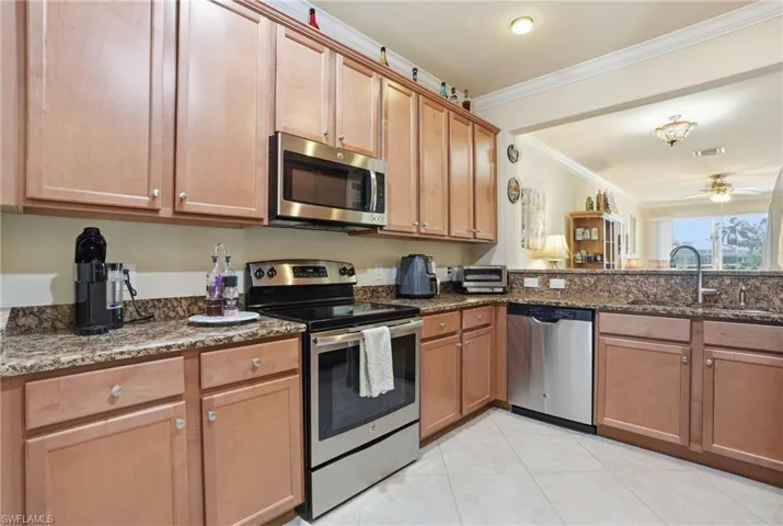 Kitchen with stainless steel appliances, dark stone countertops, wood finish cabinetry, ceiling fan, and ornamental molding