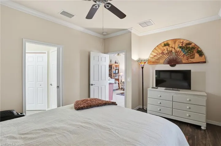 Bedroom with crown molding, a ceiling fan, and dark wood-type flooring