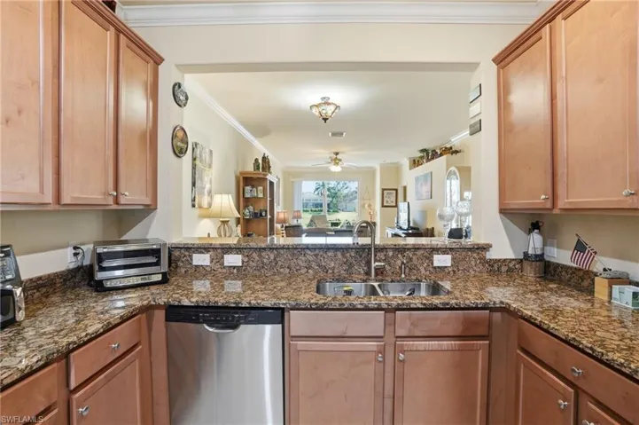 Kitchen with stainless steel dishwasher, ceiling fan, dark stone countertops, crown molding, and a peninsula