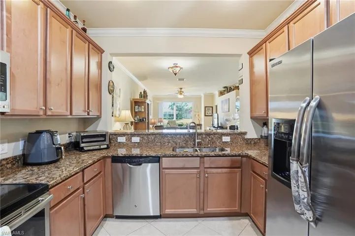 Kitchen with stainless steel appliances, dark stone countertops, crown molding, wood finish cabinetry, and a ceiling fan