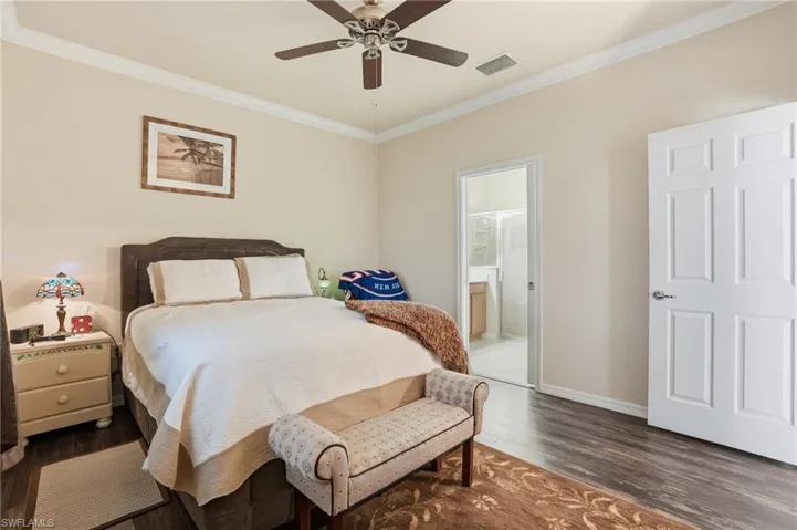Bedroom with crown molding, dark wood-type flooring, a ceiling fan, and connected bathroom