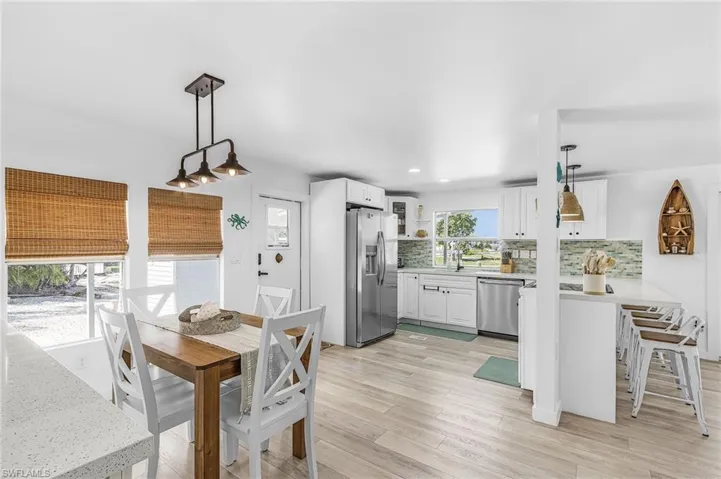 Open-concept living space with wood-finish flooring, white cabinetry, stainless steel appliances, a multi-tone tile backsplash, and a dining area with a linear pendant light