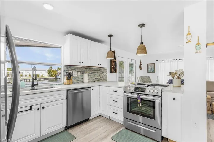 Kitchen featuring white cabinetry with black hardware, stainless steel appliances, a tile backsplash, and light wood-finish flooring