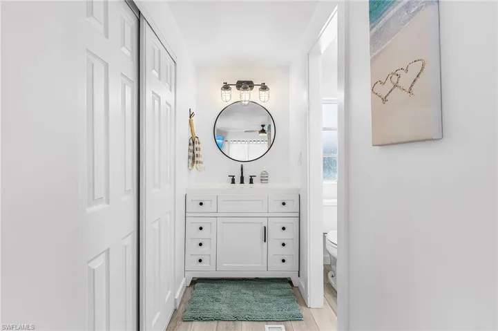 White vanity with a rectangular sink, black hardware, and a circular mirror