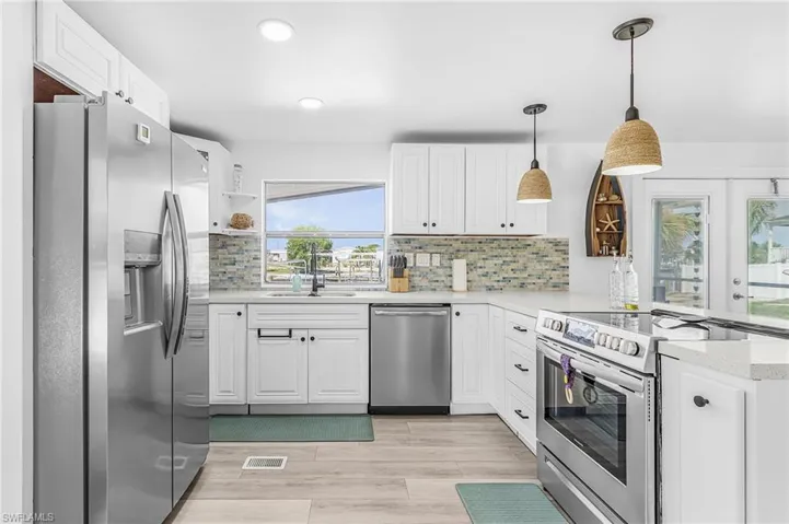Modern kitchen featuring white shaker cabinetry, stainless steel appliances, a multi-tone tile backsplash, light wood-finish flooring, and recessed lighting
