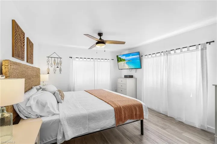Spacious room featuring wood-finish flooring, a ceiling fan, and large windows with sheer white privacy curtains