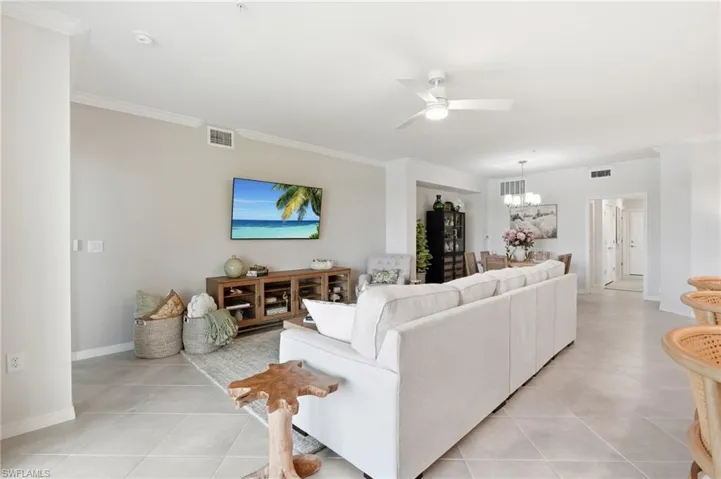 Spacious living area featuring light-toned tile flooring, crown molding, and a ceiling fan