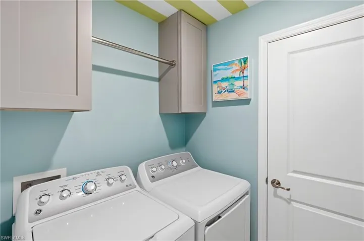 Dedicated laundry space featuring built-in cabinetry, a chrome hanging rod, and light blue wall paint