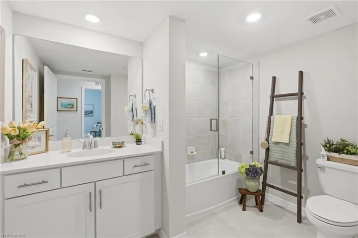 Modern bathroom featuring a single vanity with white cabinetry, a large frameless mirror, a shower-tub combination with a glass enclosure, and recessed lighting