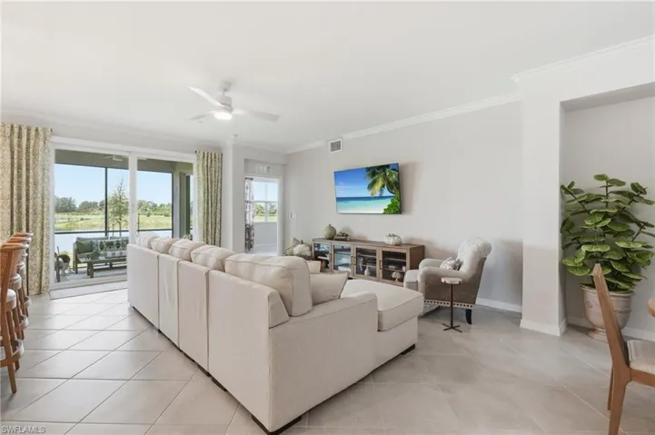 Spacious living area featuring large format tile flooring, crown molding, and a ceiling fan