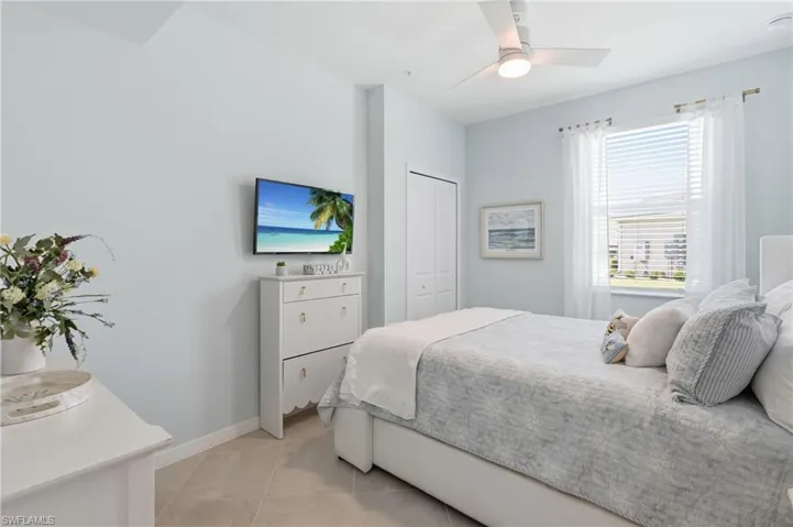 Bright bedroom featuring tiled flooring, a ceiling fan with integrated lighting, and a large window with white blinds and sheer curtains