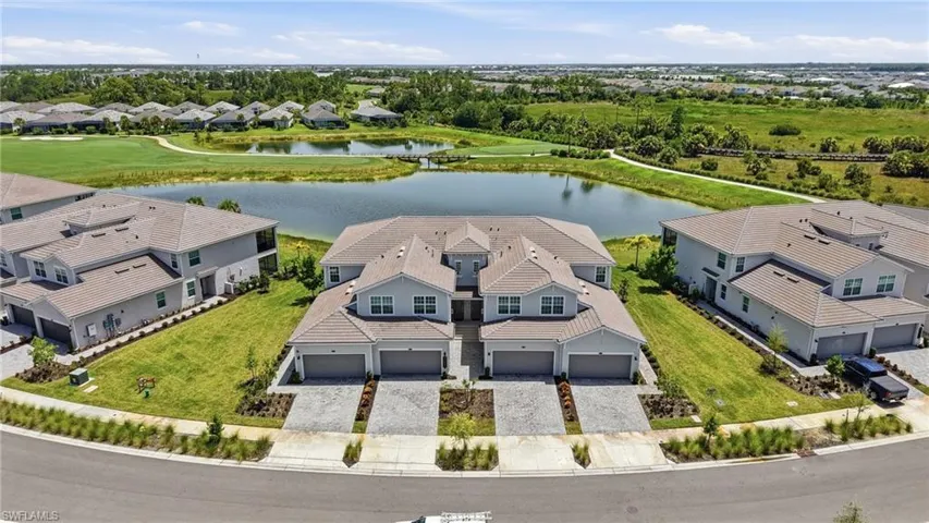 Modern townhome community featuring a large pond, expansive green spaces, paved driveways, and two-story residences with attached garages