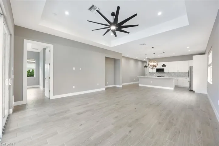 Unfurnished living room featuring light wood-type flooring, a tray ceiling, and ceiling fan