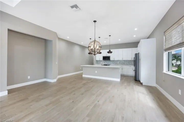 Kitchen featuring light wood-type flooring, white cabinets, a center island with sink, appliances with stainless steel finishes, and decorative light fixtures