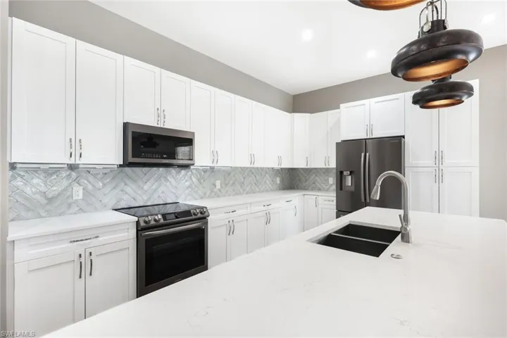 Kitchen with appliances with stainless steel finishes, tasteful backsplash, sink, and white cabinets