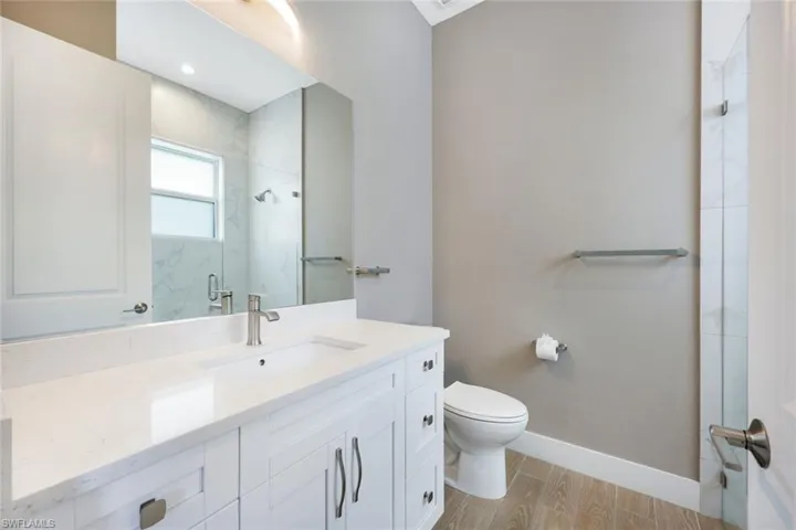 Bathroom featuring wood-type flooring, vanity, a shower with shower door, and toilet