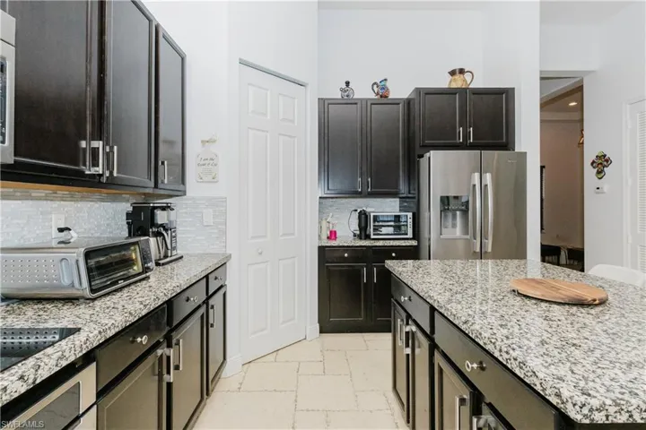 Kitchen featuring stainless steel fridge with ice dispenser, stone tile flooring, decorative backsplash, light stone countertops, and a kitchen island