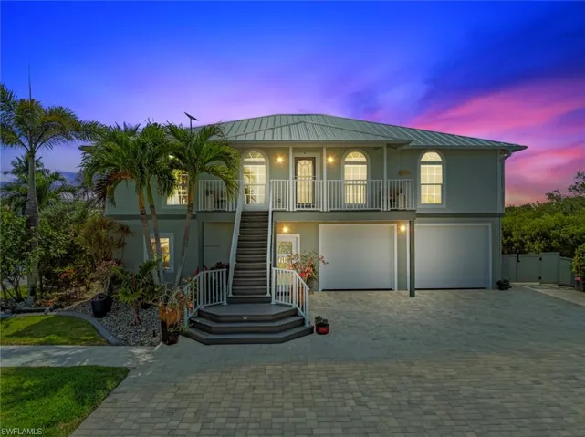 Coastal home with a garage, covered porch, stucco siding, metal roof, and stairway