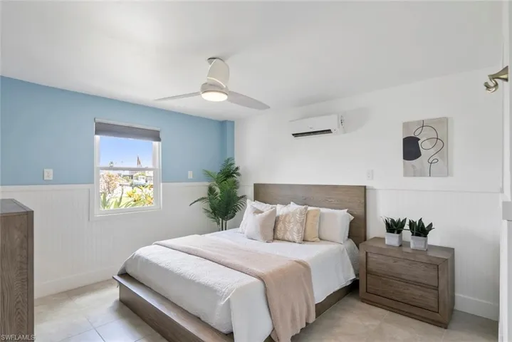 Bedroom with baseboards, ceiling fan, an AC wall unit, a wainscoted wall, and light tile patterned floors