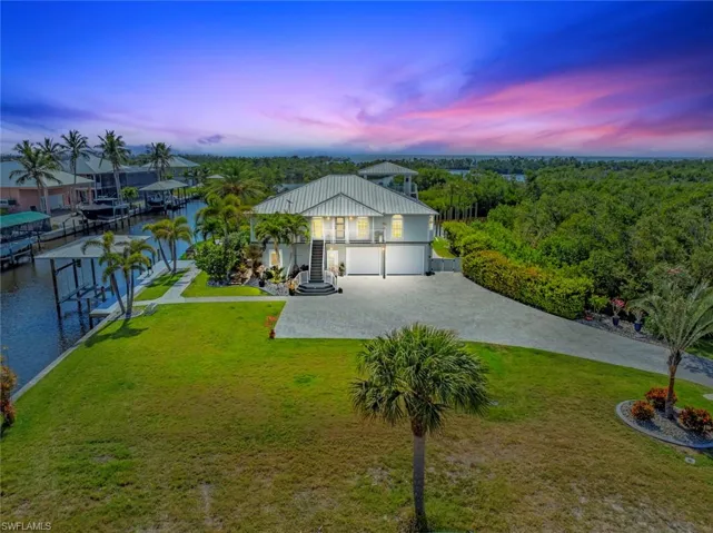 View of front of home with driveway, a lawn, boat lift, a water view, and stucco siding