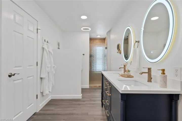 Full bathroom with double vanity, tiled shower, a sink, and wood finished floors