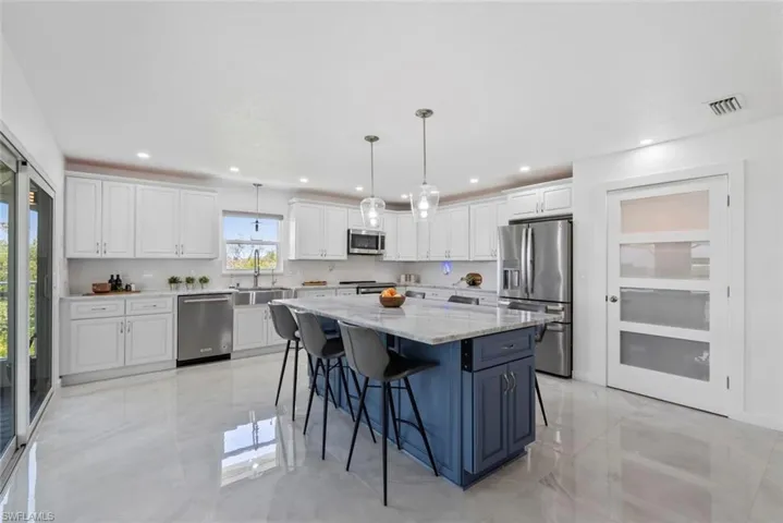 Kitchen featuring white cabinets, a sink, stainless steel appliances, a kitchen island, and visible vents
