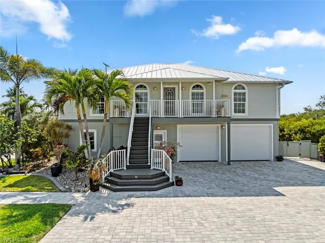 Coastal inspired home featuring an attached garage, decorative driveway, metal roof, a porch, and stairway