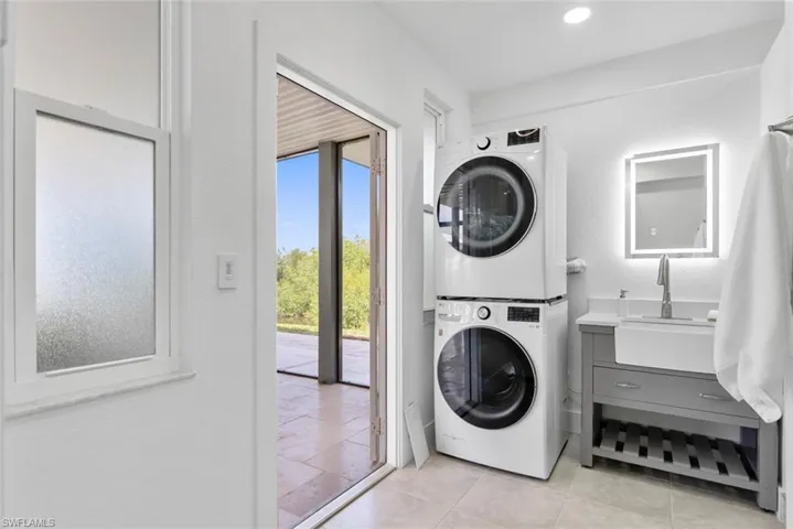 Laundry area with light tile patterned floors, laundry area, a sink, and stacked washer / dryer