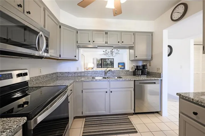 Kitchen featuring appliances with stainless steel finishes, gray cabinets, a chandelier, light stone countertops, and ceiling fan