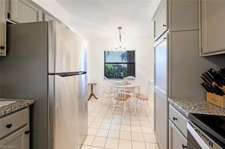 Kitchen featuring appliances with stainless steel finishes, light tile patterned floors, a chandelier, decorative light fixtures, and stone countertops
