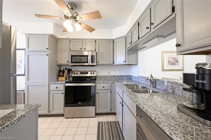 Kitchen with appliances with stainless steel finishes, gray cabinets, a ceiling fan, and light stone counters