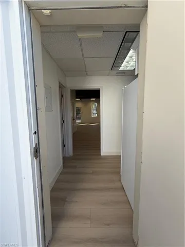 Corridor with light wood-style floors, a paneled ceiling, and electric panel