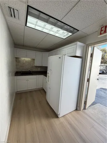 Kitchen with refrigerator, light wood-style floors, tasteful backsplash, white cabinets, and a paneled ceiling
