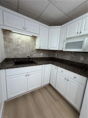 Kitchen with white cabinets, light wood finished floors, dark stone countertops, a paneled ceiling, and decorative backsplash
