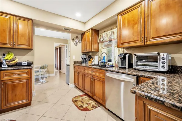 Kitchen with a toaster, dishwasher, brown cabinets, a sink, and light tile patterned floors