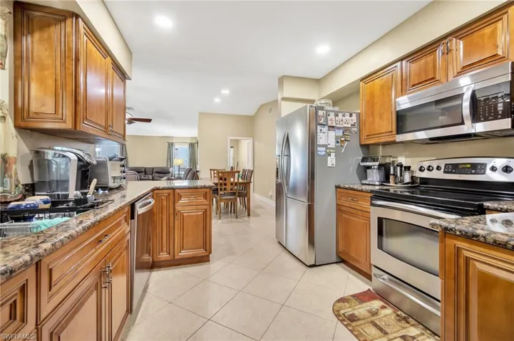 Kitchen with light tile patterned floors, stainless steel appliances, dark stone countertops, a peninsula, and brown cabinetry