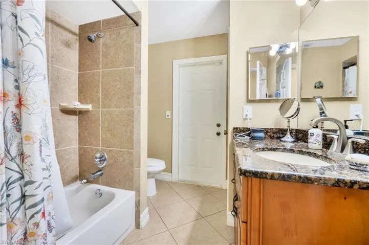 Full bathroom with toilet, vanity, shower / tub combo, tile patterned flooring, and baseboards