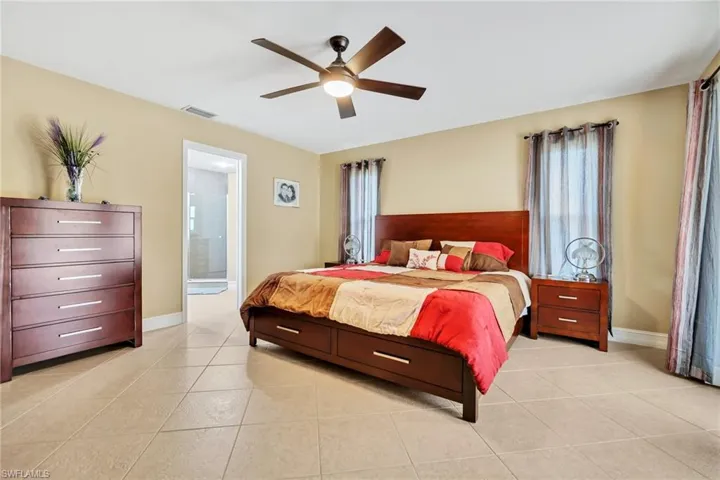 Bedroom featuring light tile patterned flooring, visible vents, baseboards, connected bathroom, and a ceiling fan